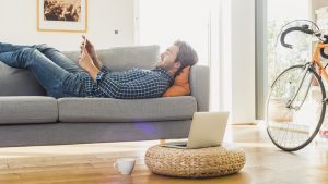 Young man lying on the couch at home looking at digital tablet; Shutterstock ID 382387387; PO: redownload; Job: redownload; Client: redownload; Other: redownload